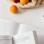Top view of opened textbooks on white table arranged with magazines and cotton sack with organic ripe apricots