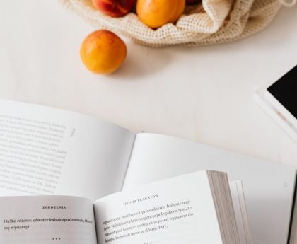 Top view of opened textbooks on white table arranged with magazines and cotton sack with organic ripe apricots