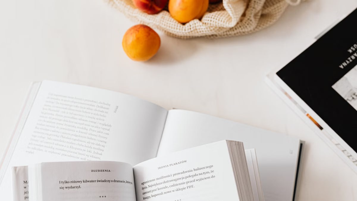 Top view of opened textbooks on white table arranged with magazines and cotton sack with organic ripe apricots