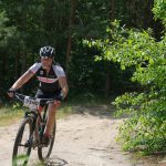 Cyclist on a mountain bike navigating a lush forest trail during a daytime race.