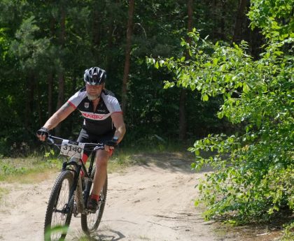 Cyclist on a mountain bike navigating a lush forest trail during a daytime race.