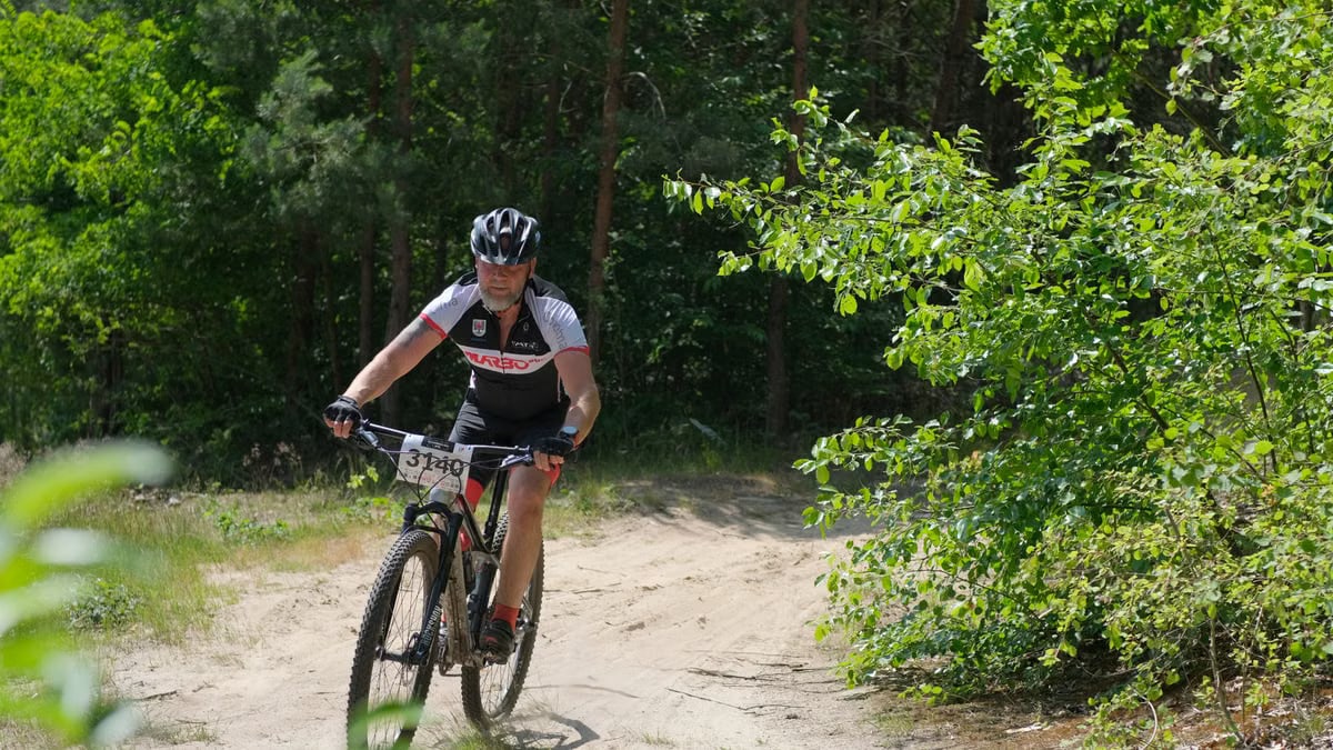 Cyclist on a mountain bike navigating a lush forest trail during a daytime race.